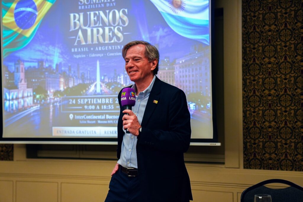 Palestrante em frente ao telão com a identidade visual de Buenos Aires no Brazilian Summit Day — Turnê Buenos Aires 2026