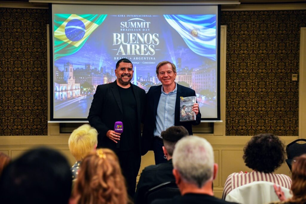 Dois participantes posam no palco com o telão do evento ao fundo no Brazilian Summit Day — Turnê Buenos Aires 2026