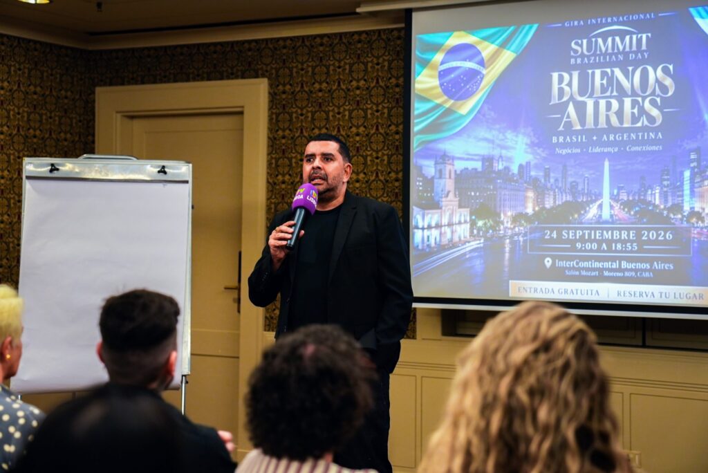Apresentador fala ao microfone com o telão do evento ao fundo no Brazilian Summit Day — Turnê Buenos Aires 2026